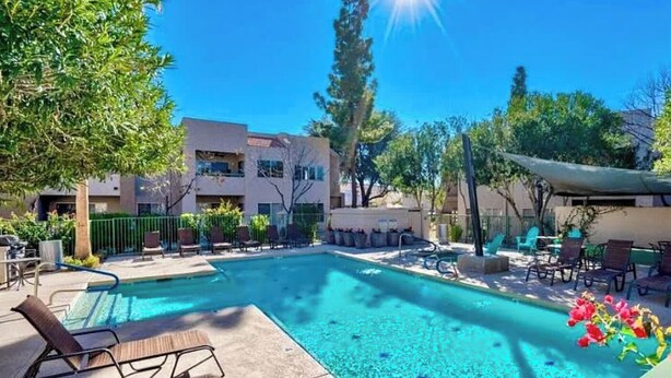 A swimming pool with lounge chairs, surrounded by greenery and a building. - Charming condo in Downtown Gilbert (Gilbert)