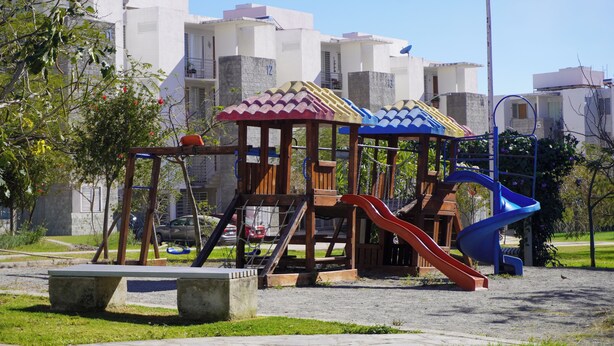 A playground with slides and swings, surrounded by buildings and a street lamp.