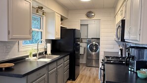Una cocina moderna con armarios grises, un refrigerador negro, una lavadora y un microondas.