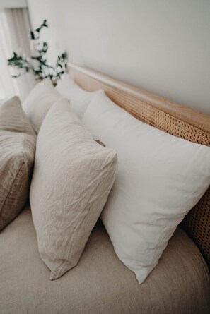 Un lit avec une tête de lit en bois, une literie de couleur beige et une plante en arrière-plan.