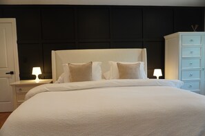 A neatly made bed with white linens, a dark headboard, and a white nightstand with a lamp. - Spacious 4-bedroom house 9 Miles Boston/Train-3mi/Airport-6mi/+Parking (Malden)