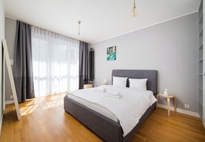 A modern bedroom with a large bed, a bedside table, a nightstand, and a window with curtains. - Mokotowska Homely Apartment (Warszawa)