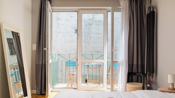 Ein Hotelzimmer mit Bett, einem Fenster mit Vorhängen, einem Balkon mit Stühlen und einer Lampe.