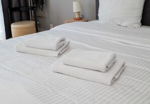 A neatly made bed with folded white towels, a bedside lamp, and a chair. - Mokotowska Homely Apartment (Warszawa)