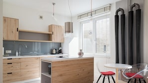 Eine moderne Küche mit Holzschränken, einer weißen Arbeitsplatte, einem Edelstahl-Spülbecken und einem Essbereich mit weißem Tisch und roten Stühlen.