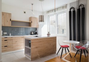 A modern kitchen with wooden cabinets, a white countertop, a stainless steel sink, and a dining area with a white table and red chairs. - Mokotowska Homely Apartment (Warszawa)