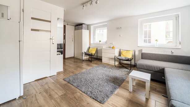 A modern living room with a sofa, chairs, a coffee table, and a large window providing natural light. - Old Town Harmony Studio (Poznań)