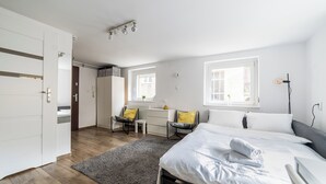 A bedroom with a bed, bedside table, chair, desk, wardrobe, and a large window. - Old Town Harmony Studio (Poznań)