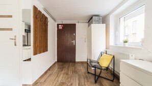 A hallway with a wooden floor, a white door, a coat rack, a radiator, and a window. - Old Town Harmony Studio (Poznań)