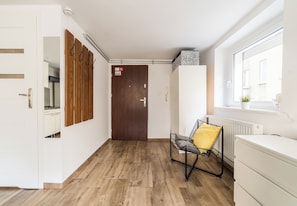 A hallway with a wooden floor, a white door, a coat rack, a radiator, and a window. - Old Town Harmony Studio (Poznań)