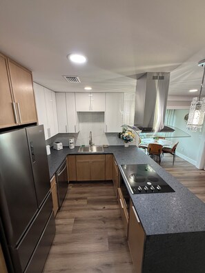 A modern kitchen with built-in appliances, a central island, and a dining area with a chandelier. - Luxury Coastal Condo • Fully Renovated•Near Beach (Destin)