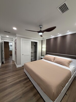 Ein Schlafzimmer mit einem Bett, einem Deckenventilator, einem Nachttisch, einer Wandleuchte und einem Holzboden.