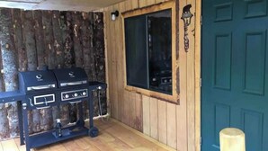 A wooden exterior wall with a blue door, a window, and a barbecue grill. - Lovely 1-bedroom cabin in Anchor Point perfect for a cozy getaway (Anchor Point)