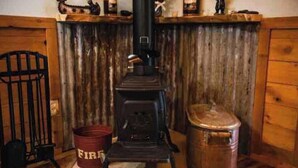 A rustic room with a wood-burning stove, a metal bucket, and a wooden cabinet. - Lovely 1-bedroom cabin in Anchor Point perfect for a cozy getaway (Anchor Point)