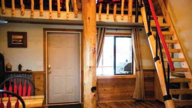 A wooden interior with a door, a window with curtains, a chair, and a wooden staircase. - Lovely 1-bedroom cabin in Anchor Point perfect for a cozy getaway (Anchor Point)