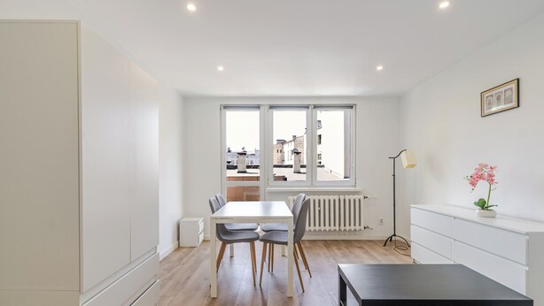 Una habitación moderna y bien iluminada con una mesa de comedor, sillas, un radiador y vistas amplias a través de grandes ventanas.