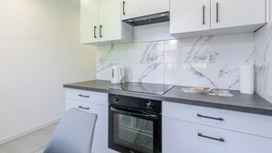 Una cocina moderna con armarios blancos, horno integrado y una encimera de mármol.