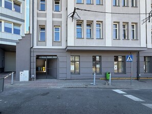 Ein modernes Gebäude mit Eingang im Erdgeschoss, einem Fußgängerübergang-Schild und einer grünen Mülltonne.