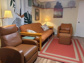 Ein Wohnzimmer mit einem braunen Ledersofa, einem passenden Sessel, einem Holztisch und einem roten Teppich.
