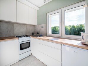 Eine Küche mit weißen Schränken, einem Gasherd, einem Backofen, einer Spüle und einem Fenster mit Blick auf Grünflächen.