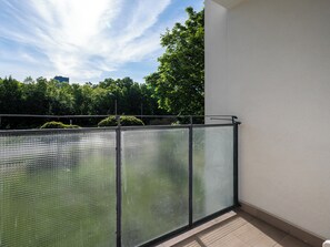Ein Balkon mit Metallgeländer, Blick auf Bäume und ein Gebäude im Hintergrund.