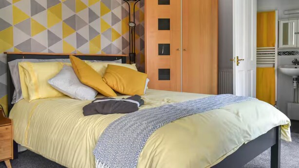 Une chambre à coucher avec un lit, une armoire, une lampe de chevet et une salle de bain visible à travers une porte ouverte.