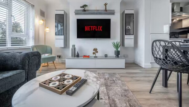 En moderne stue med et fladskærms-tv, en sofa, et sofabord og et spiseområde med en stol.