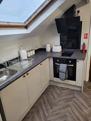 Eine kleine Küche mit Dachfenster, einer Spüle, einem Wasserkocher, einem Toaster und einem Feuerlöscher.