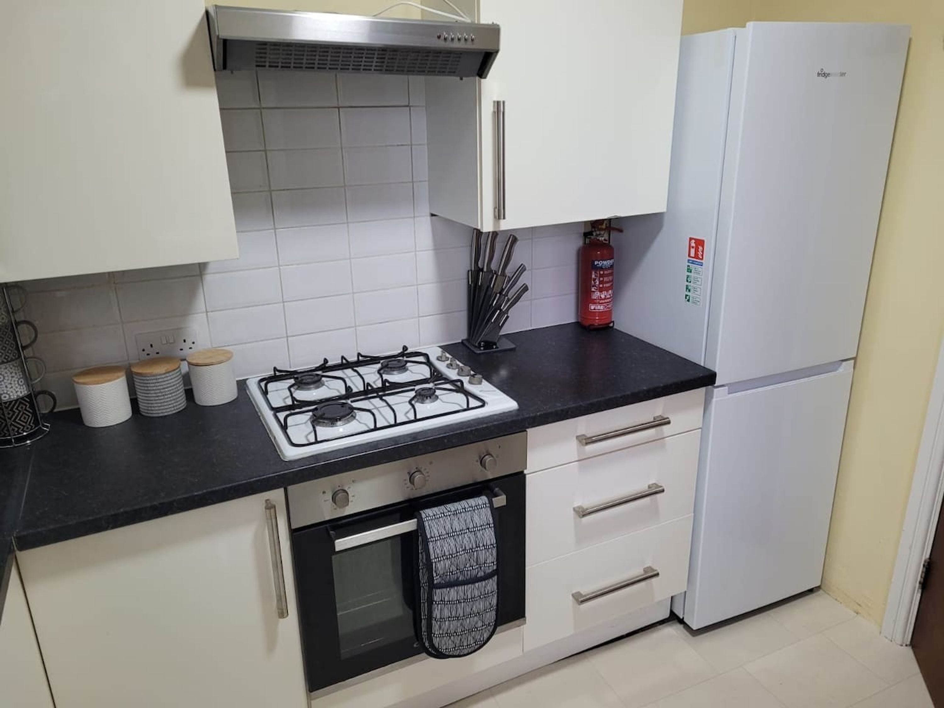 A kitchen with a gas stove, oven, white cabinets, and a white refrigerator.