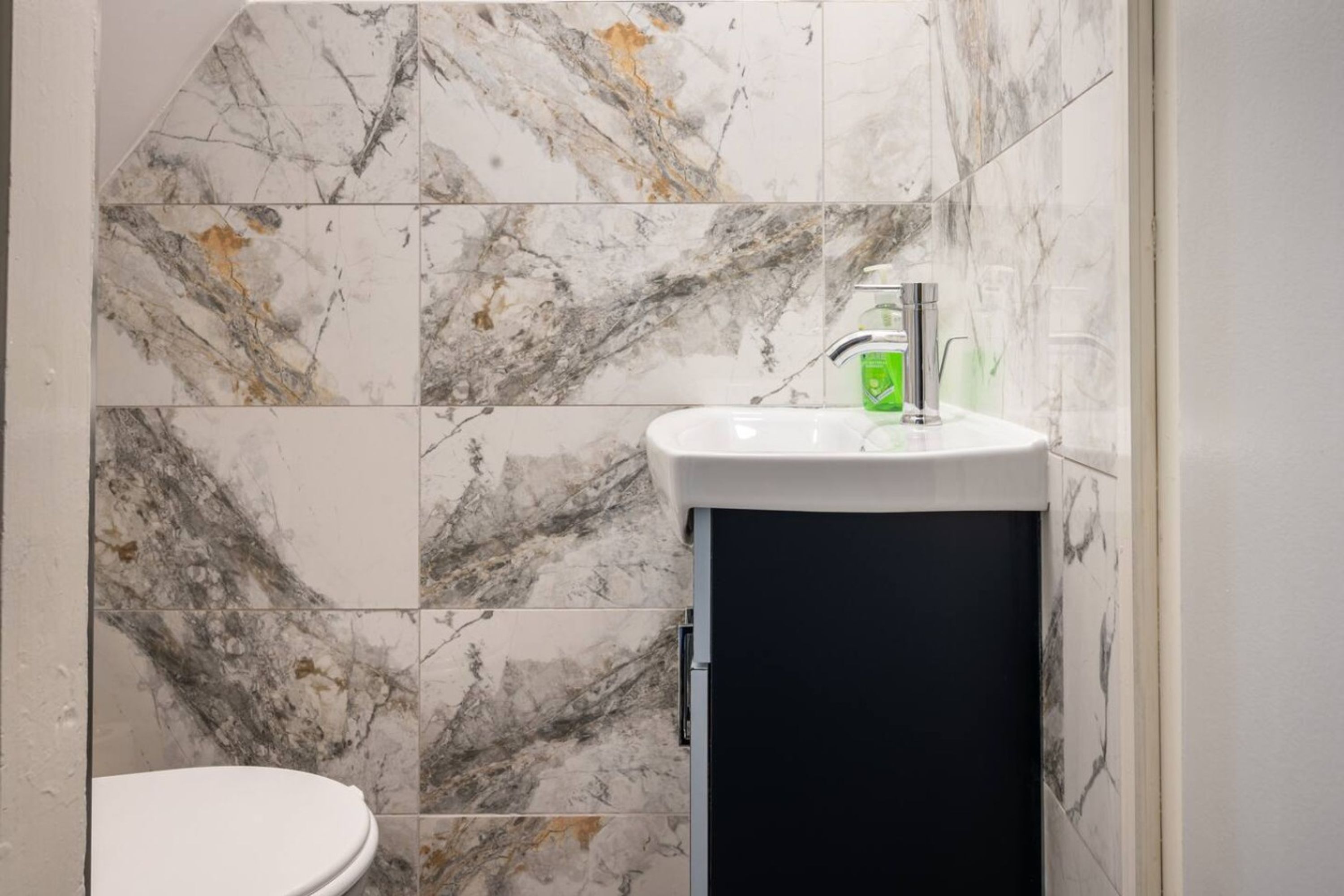 A bathroom with a white toilet, a black cabinet, and a sink with a green soap dispenser.