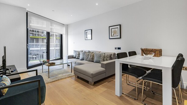 Een moderne woonkamer met een bank, een eettafel en stoelen. Er is een glazen deur die naar een balkon leidt.