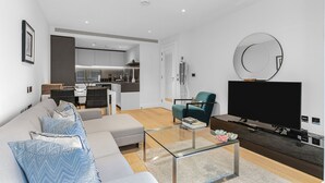 Een moderne woonkamer met een bank, salontafel en televisie. Achtergrond toont een keuken.