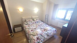 Un dormitorio con cama, mesitas de noche, un radiador y una ventana.
