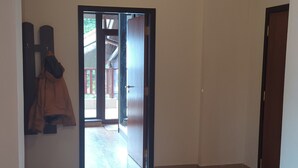 Un pasillo amplio con suelo de baldosas, una escalera de madera y una puerta que da al exterior.