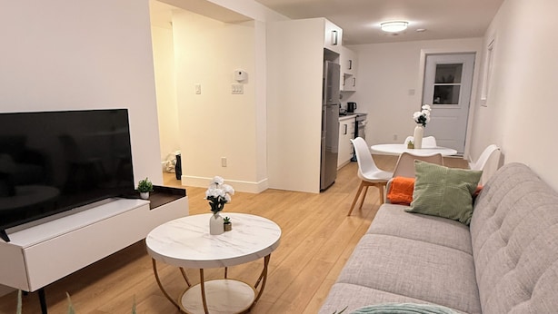 Ein modernes Wohnzimmer mit Flachbildfernseher, rundem Couchtisch, einer Couch mit Kissen und einem Essbereich mit Tisch und Stühlen.