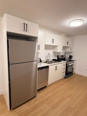 A modern kitchen with white cabinets, stainless steel appliances, and a wooden floor.