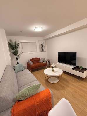 A modern living room with a grey sofa, a red couch, a round coffee table, a flat-screen TV, and a small side table.