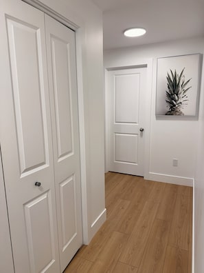 Un couloir avec des portes blanches, un plancher en bois et un tableau encadré accroché au mur.