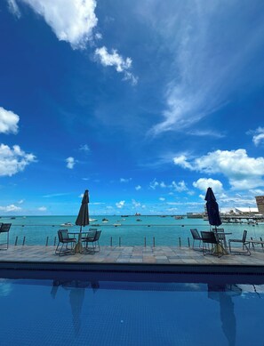A poolside view with chairs and umbrellas, a clear sky, and a distant view of boats and buildings. - Apartment for 6 People - Oceanfront (Fortaleza)