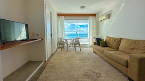 Ein Wohnzimmer mit Fernseher, einer Couch, einem Esstisch mit Stühlen und Meerblick durch ein großes Fenster.