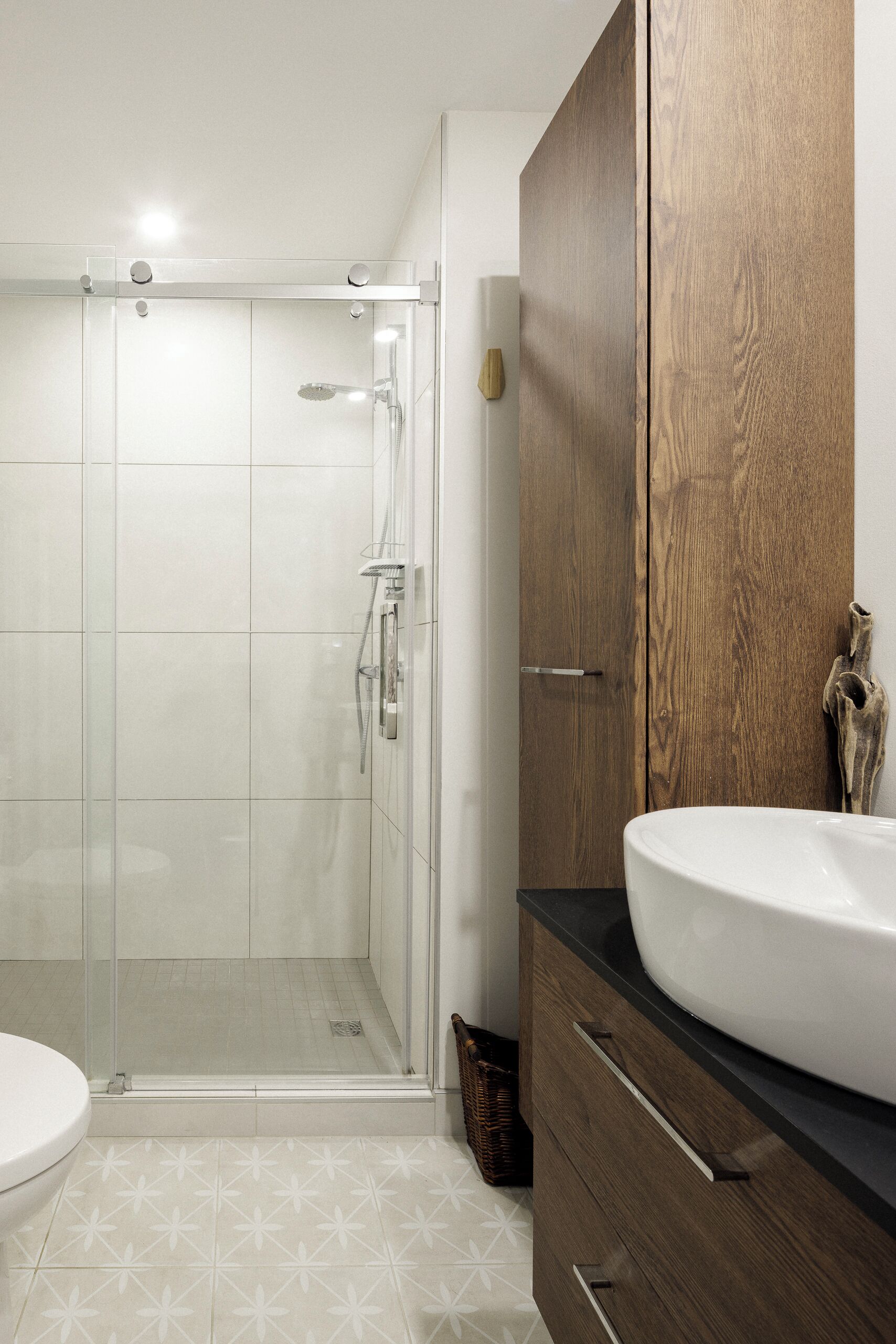 Une salle de bain avec une douche à parois de verre, un lavabo blanc et des meubles en bois.