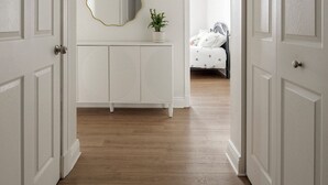 Un pasillo con puertas blancas, un tocador blanco con espejo y una cama al fondo.