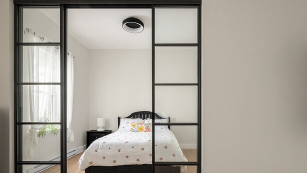 Un dormitorio con cama, mesita de noche, lámpara y ventana con cortinas.