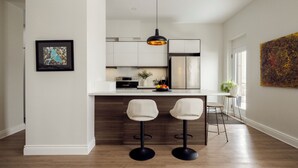 Una cocina moderna con gabinetes blancos, un colgante negro y dos taburetes de bar.