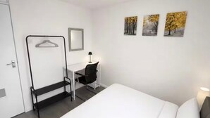 Ein Hotelzimmer mit einem Bett, einem Schreibtisch mit Stuhl, einem Kleiderhaken und drei Wandbildern.