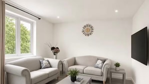 Ein modernes Wohnzimmer mit zwei Sofas, einem Couchtisch, einem Beistelltisch, einem wandmontierten Fernseher und einer dekorativen Sonnenstrahlleuchte.