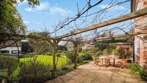 A patio with a wooden pergola, a round table, and chairs, surrounded by a garden and a brick wall. - Villa Sleeps up to 17 - Hot Tub, Garden, Parking (Pinner)