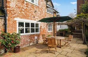 Une maison en briques avec un patio, une table entourée de chaises et un parasol vert.