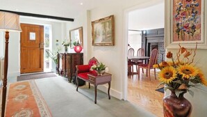 A spacious living room with a wooden door, a red sofa, a dining table with chairs, and a vase of sunflowers. - Villa Sleeps up to 17 - Hot Tub, Garden, Parking (Pinner)