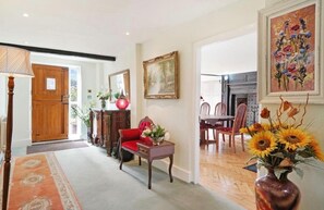 A spacious living room with a wooden door, a red sofa, a dining table with chairs, and a vase of sunflowers. - Grade 2 listed 20 mins to Baker street sleeps 17 (Pinner)